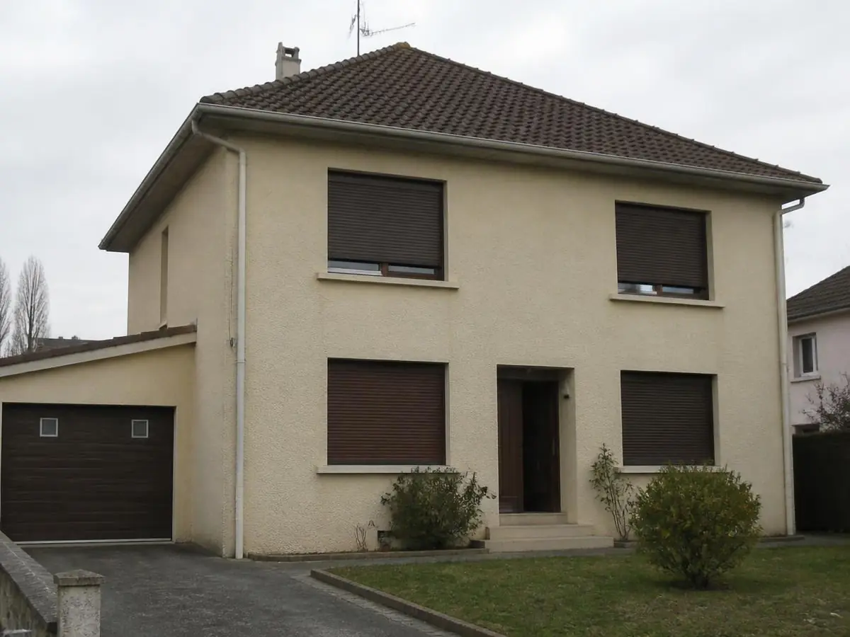 Maison à étage à l’enduit beige, volets roulants bruns et garage attenant